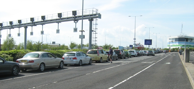 a queue of cars ina long line with buildings and various lanes at the channel tunnel terminal england